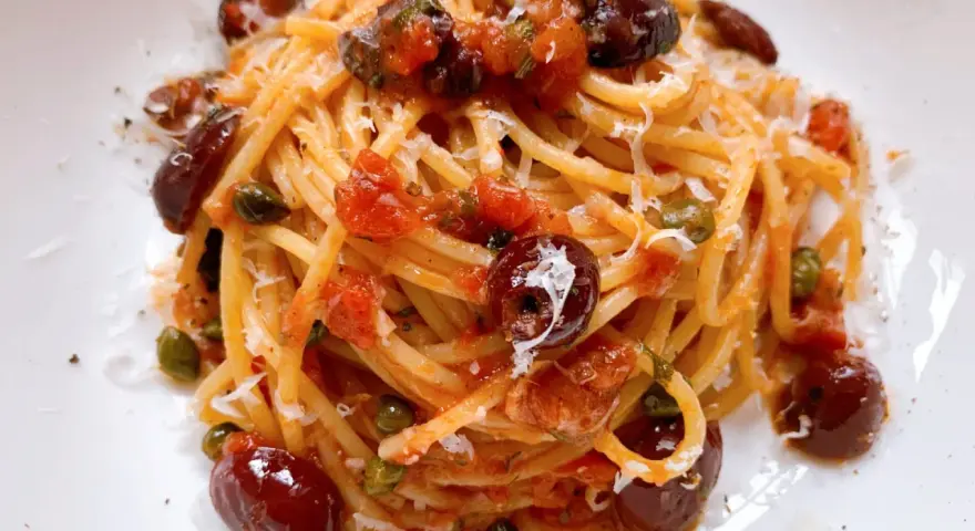 Ein Teller Spaghetti Puttanesca, garniert mit Oliven, Kapern und Parmesan.
