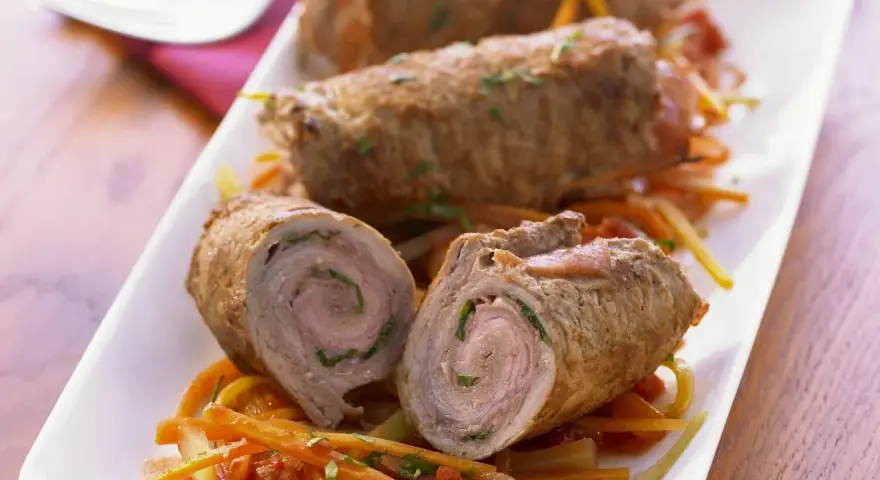 Drei köstliche kalbsrouladen italienisch auf einem Bett aus Gemüse. Eines ist aufgeschnitten und zeigt die saftige Füllung.