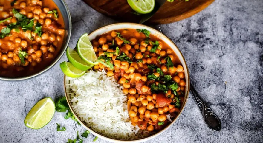 Herzhafte Kichererbsen Rezepte: Ein Teller mit Reis und Kichererbsen-Curry, garniert mit Limettenspalten und Koriander.