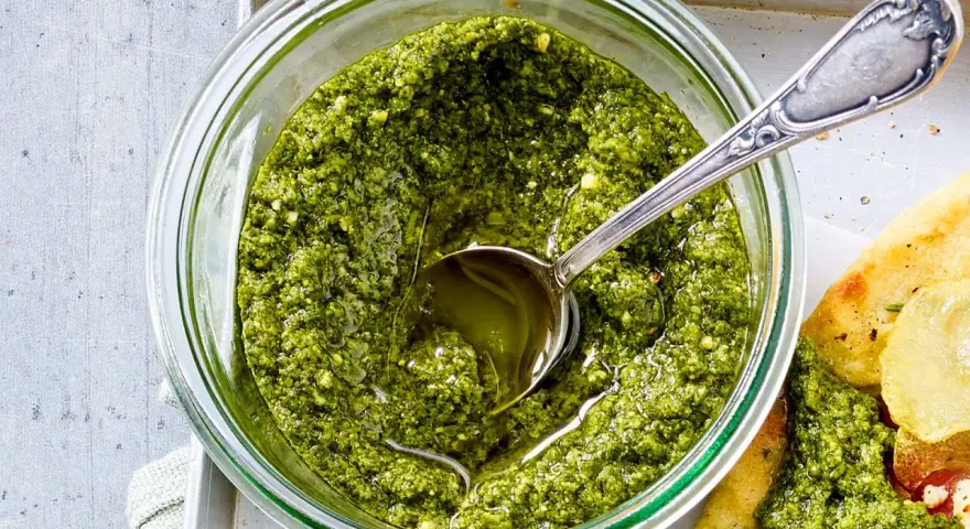 Frisches Basilikum Pesto in einem Glas, mit einem Löffel darin. Perfekt für Pasta oder Bruschetta.