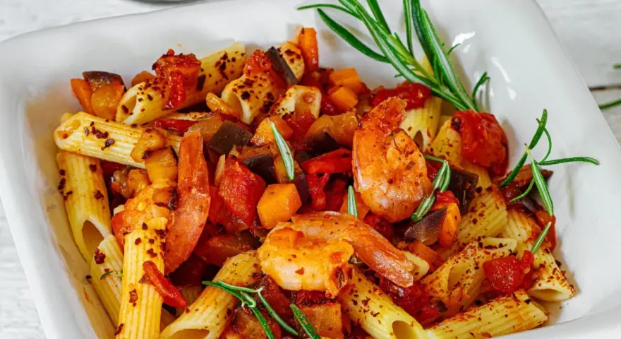 Penne-Nudeln mit Garnelen, Auberginen und Tomaten, garniert mit Rosmarin und Chiliflocken. Ein köstliches Gericht, das Lust auf mehr macht.