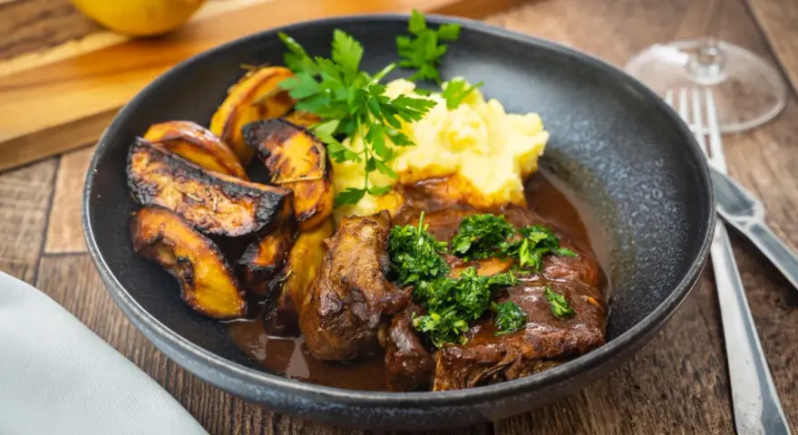 Herzhaftes Osso Buco, eine **beinscheibe italienisch** zubereitet, serviert mit cremigem Kartoffelpüree und gerösteten Kartoffelspalten.