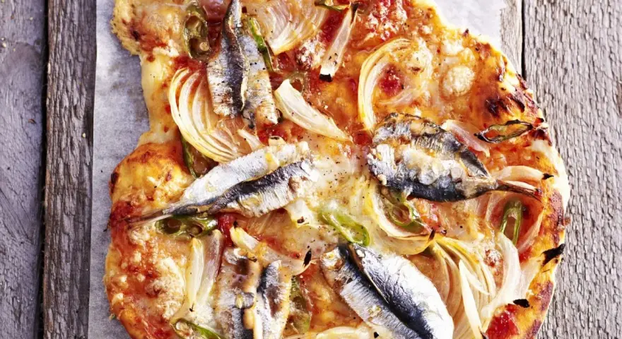 Eine rustikale Sardellen Pizza mit Zwiebeln und grünen Paprikastreifen, auf einem Holzbrett serviert.