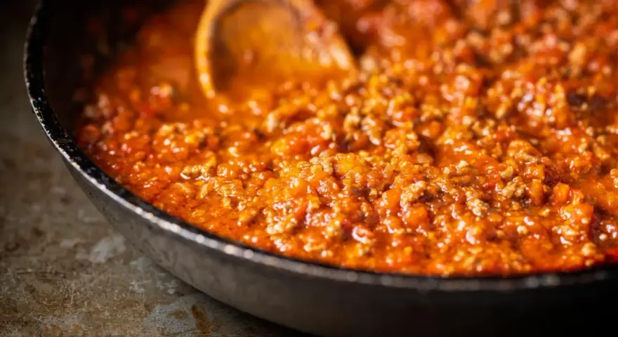Herzhafte Bolognese-Sauce köchelt in einer Pfanne, die Zutaten für ein perfektes Pastagericht. Ein Holzlöffel rührt die köstliche Masse.