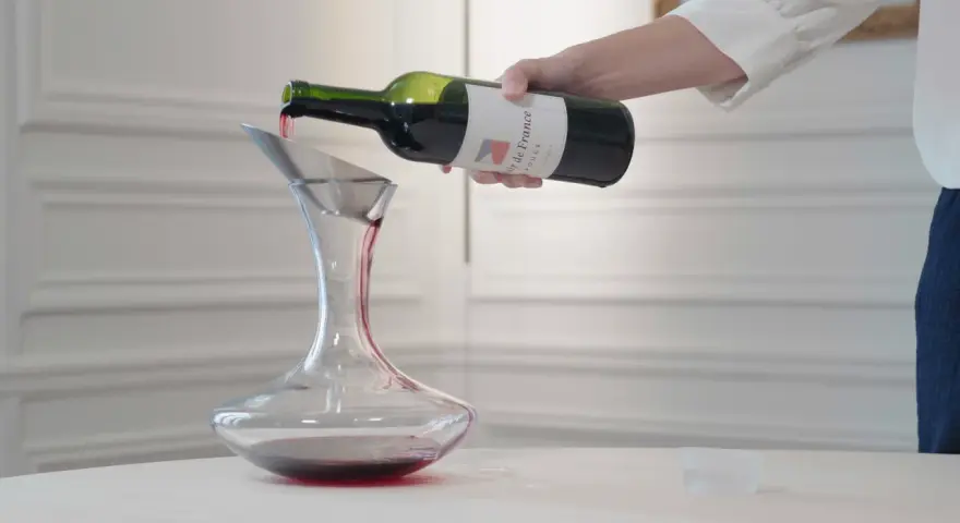 Roter Wein wird aus einer Flasche in einen Dekanter gegossen. Der Wein ist verkorkt und bereit zum Genießen.