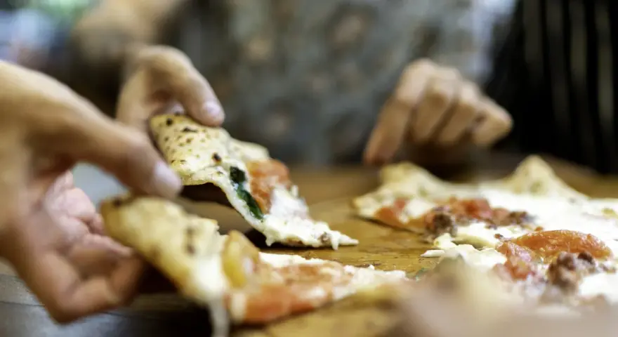 Hände greifen nach dampfenden Pizzastücken. So wie essen Italiener Pizza: gemeinsam, genussvoll, mit Freunden.