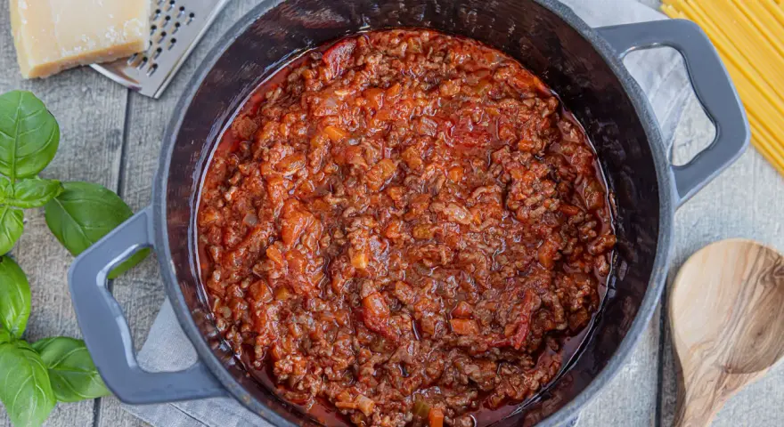 Herzhafte, beste Bolognese original im Topf, mit frischem Basilikum, Parmesan und Spaghetti daneben.
