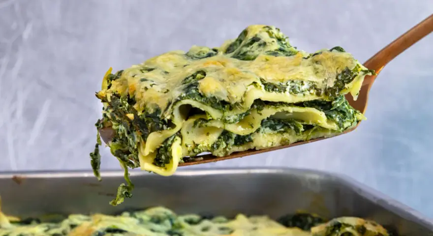 Ein Stück cremiger Ricotta Spinat Lasagne wird aus einer Auflaufform gehoben.