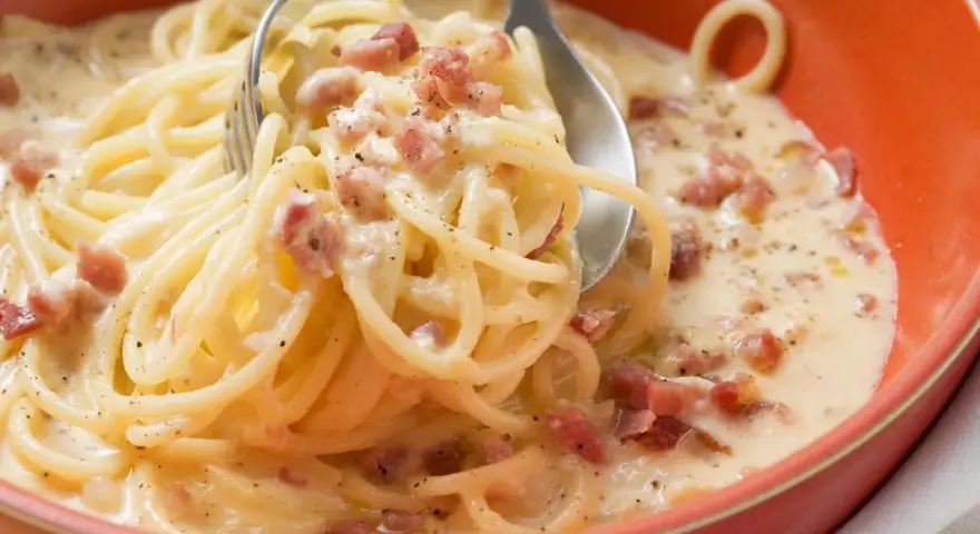 Cremige Pasta mit Ei und Speckwürfeln, ein klassisches italienisches Gericht, serviert in einer orangen Schüssel.
