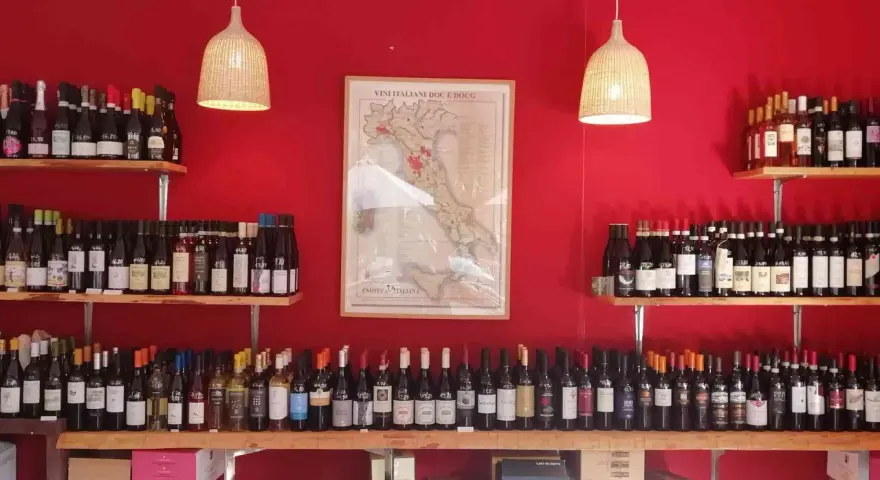 Regal voller italienischer Weinsorten vor roter Wand. Eine Karte Italiens mit Weinregionen hängt zentral.