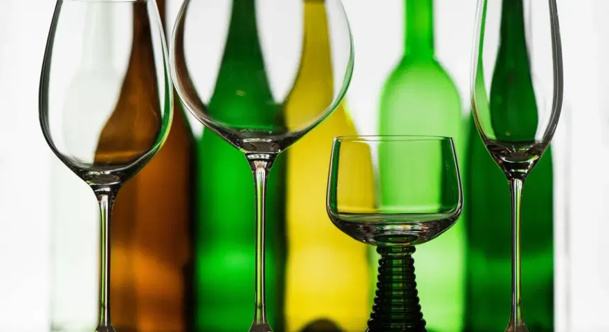 Leere Weingläser stehen vor bunten Flaschen. Perfekt, wenn man Wein kalt trinkt.