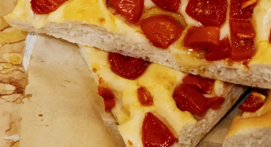 Saftige Focaccia Pomodoro mit geschmolzenem Käse und sonnengetrockneten Tomaten, auf Backpapier serviert.