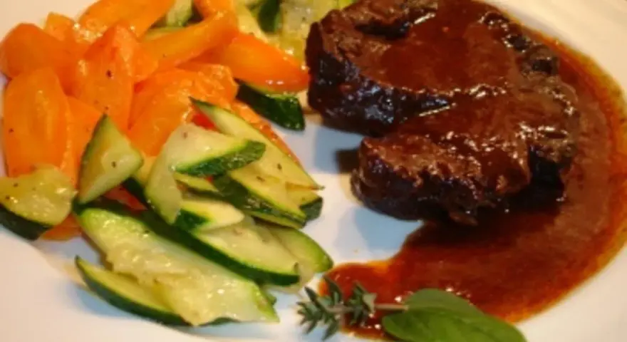 Ossobuco vom Rind auf sizilianische Art, zart geschmort in dunkler Sauce, serviert mit Karotten und Zucchini.