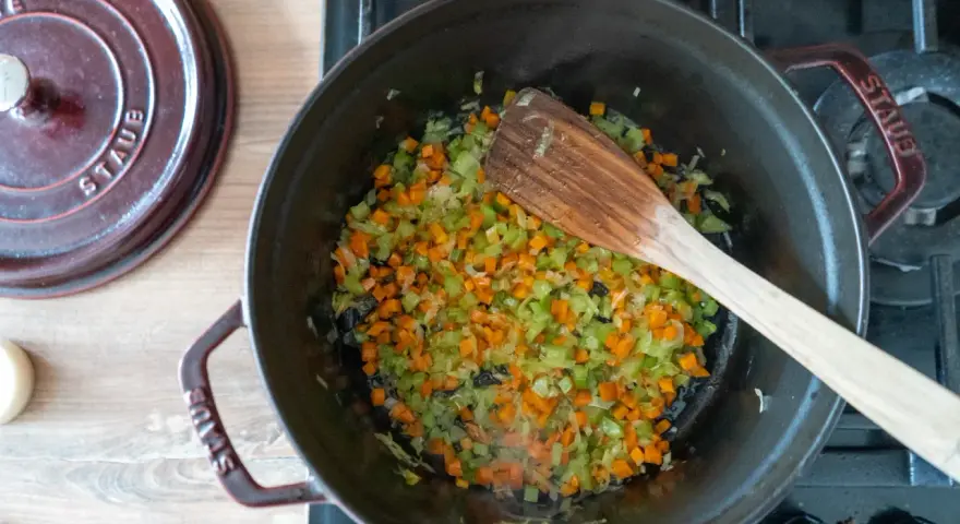 Würziges Sofrito Rezept: Karotten, Sellerie und Zwiebeln werden in einem gusseisernen Topf angedünstet.