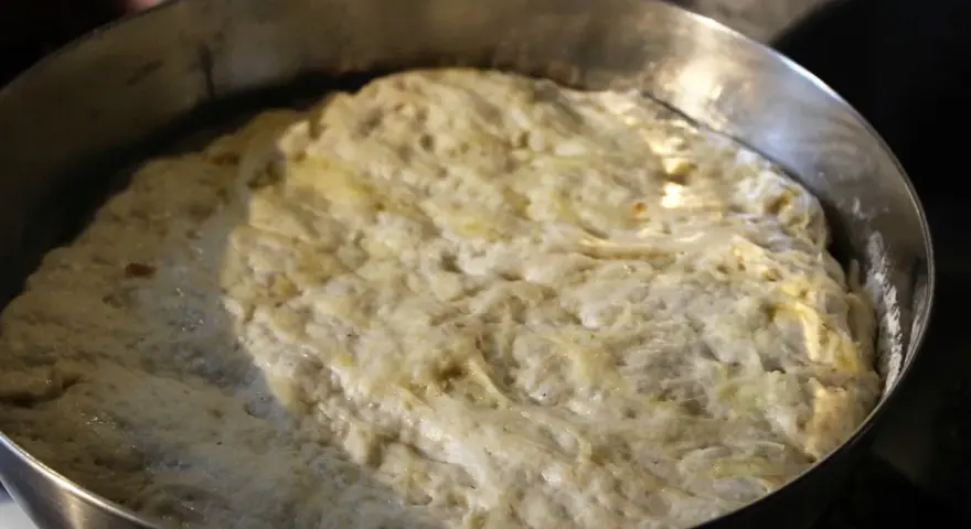 Hefeteig für Pizza geht auf. Die luftige Masse quillt über den Rand der Metallschüssel.