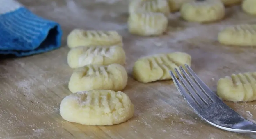 Frisch geformte italienische Gnocchi liegen auf bemehltem Holz. Eine Gabel und ein blauer Lappen sind ebenfalls zu sehen.