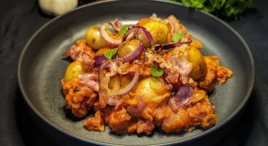Herzhafte Salsiccia-Rezepte ohne Pasta: Kartoffeln, rote Zwiebeln und Speck in einer würzigen Tomatensauce, garniert mit frischen Kräutern.