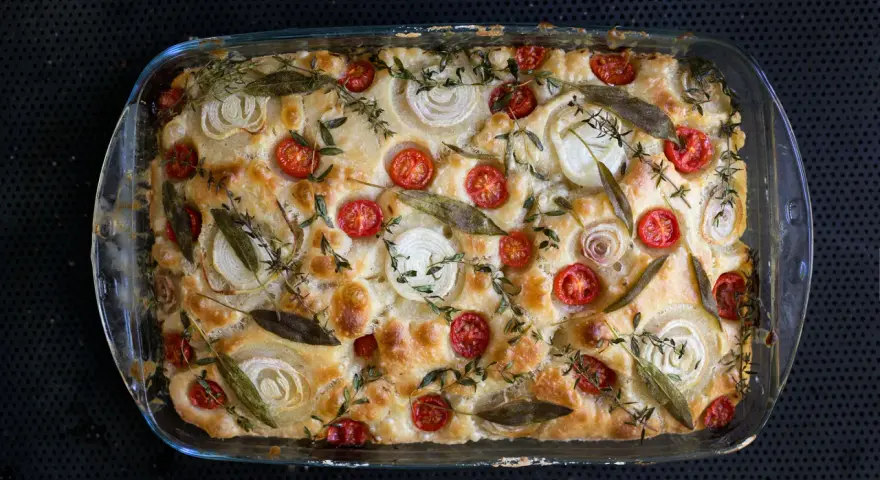 Frisch gebackene Focaccia mit Kirschtomaten, Zwiebelringen und Kräutern belegen.