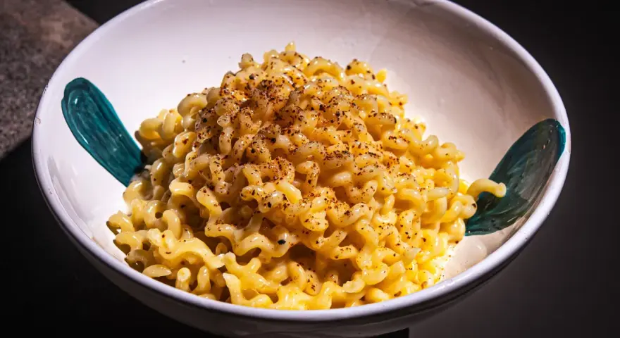 Cremige Pasta Alfredo, bestreut mit Gewürzen, in einer weißen Schüssel mit türkisfarbenen Akzenten.