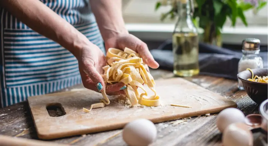Frische Pasta aus dem perfekten pasta teig rezept. Hände halten die Bandnudeln, Mehl und Eier liegen bereit.