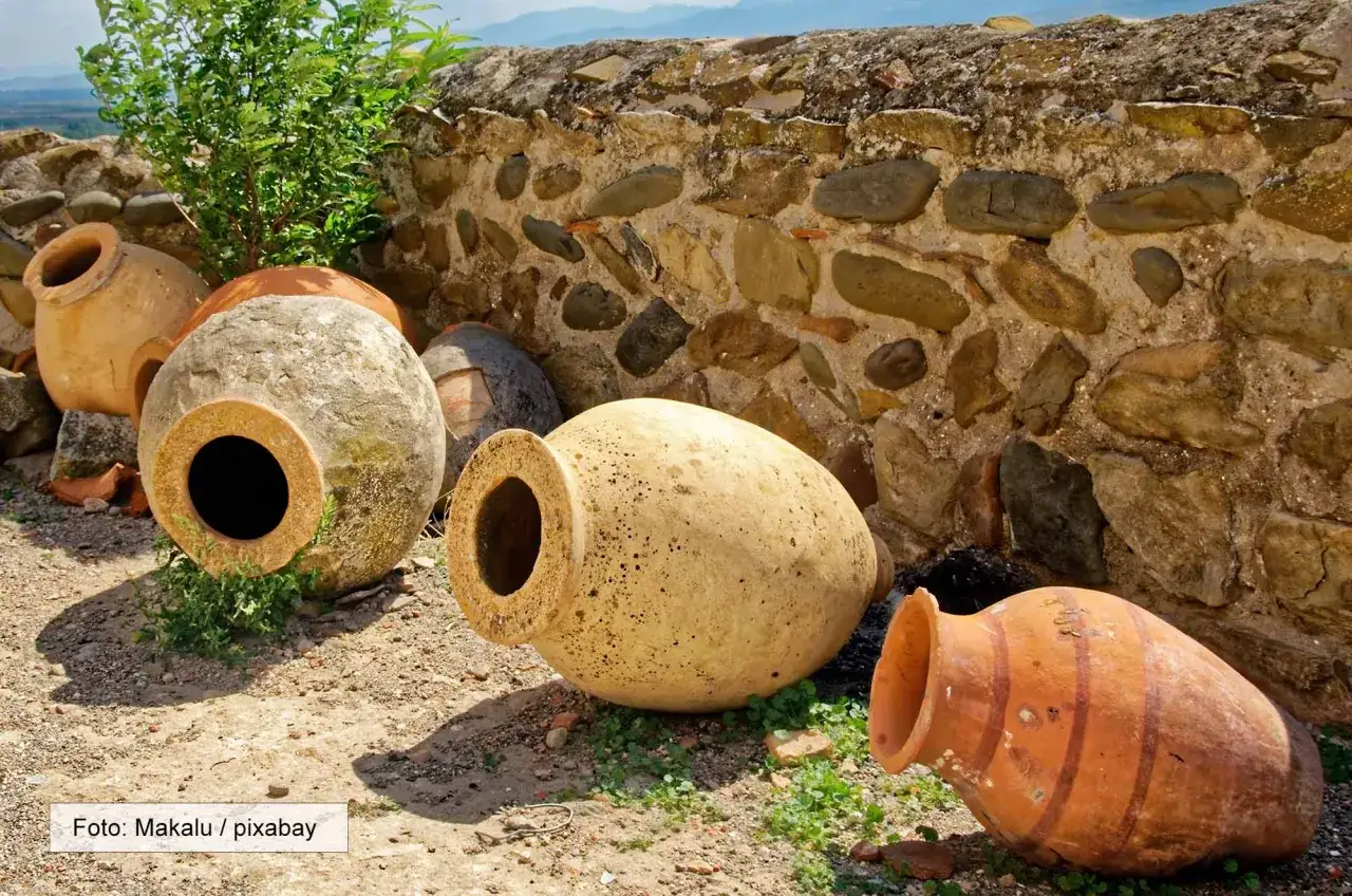 Alte Tonkr&uuml;ge, die an die Frage erinnern, wer hat Wein erfunden. Sie stehen vor einer Steinmauer.