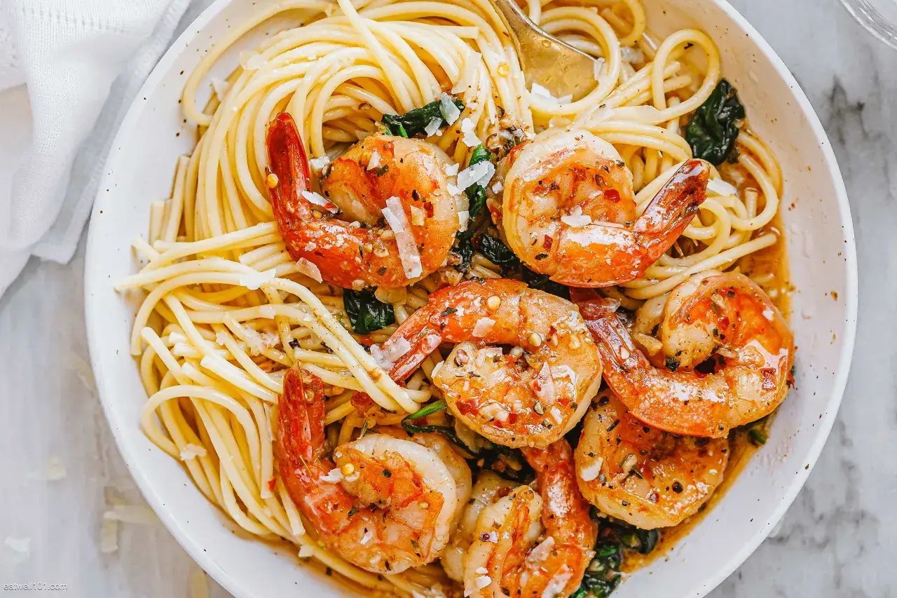 Teller mit Spaghetti mit Garnelen, garniert mit Parmesan und Kr&auml;utern. Ein goldener L&ouml;ffel ragt aus der k&ouml;stlichen Mahlzeit.