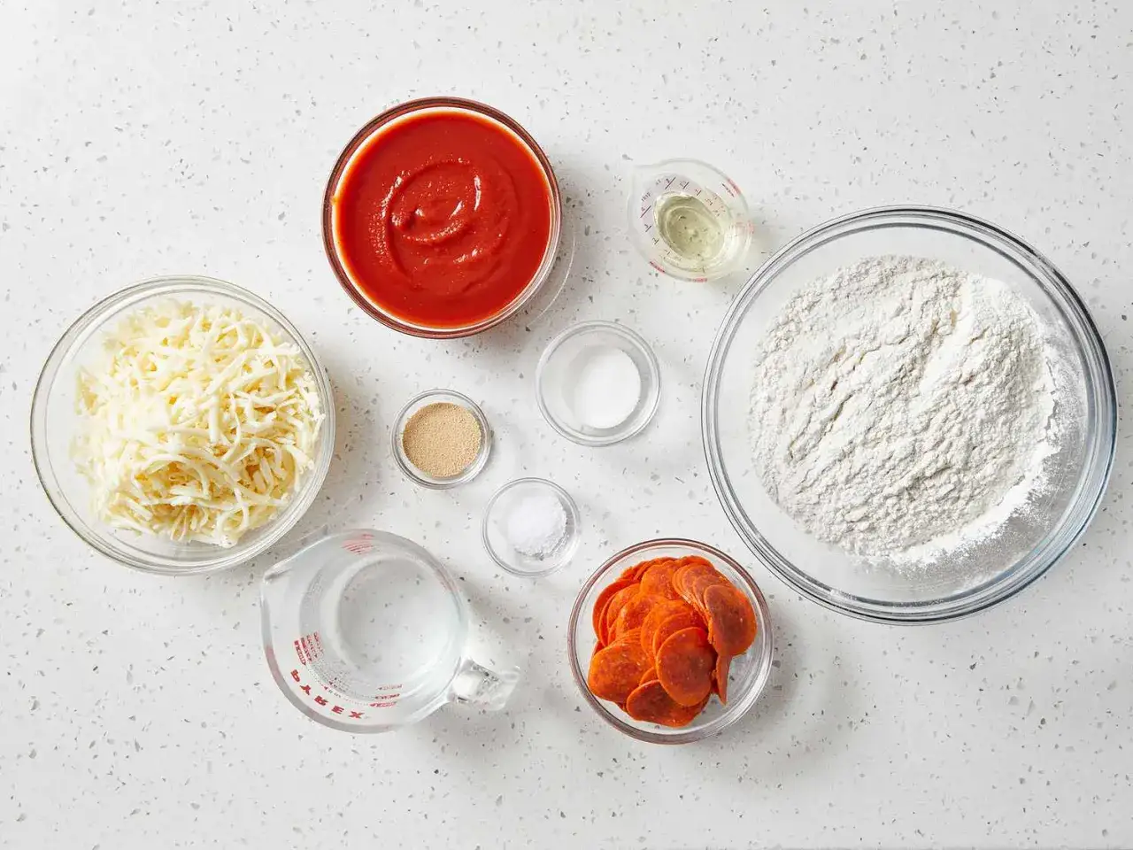 Alle Zutaten für Pizzateig: Mehl, Wasser, Hefe, Salz, Öl, Käse und Pepperoni.