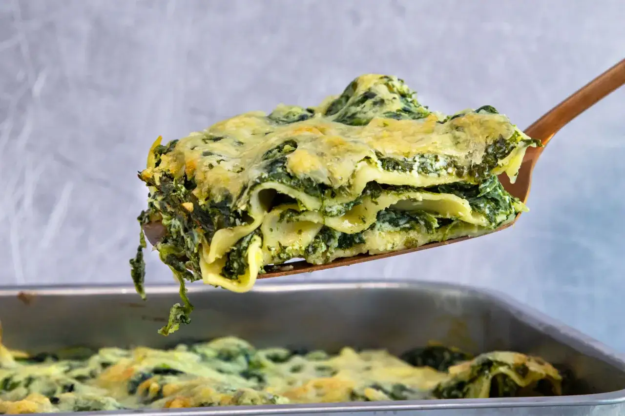 Ein St&uuml;ck cremiger Ricotta Spinat Lasagne wird aus einer Auflaufform gehoben.
