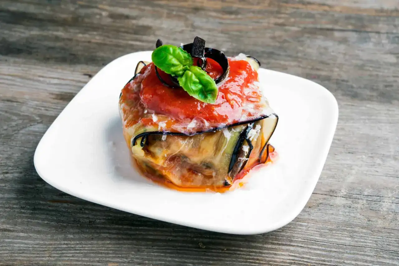 Ein k&ouml;stlicher Auberginenauflauf italienisch, geschichtet mit Tomatenso&szlig;e, K&auml;se und frischem Basilikum, serviert auf einem wei&szlig;en Teller.