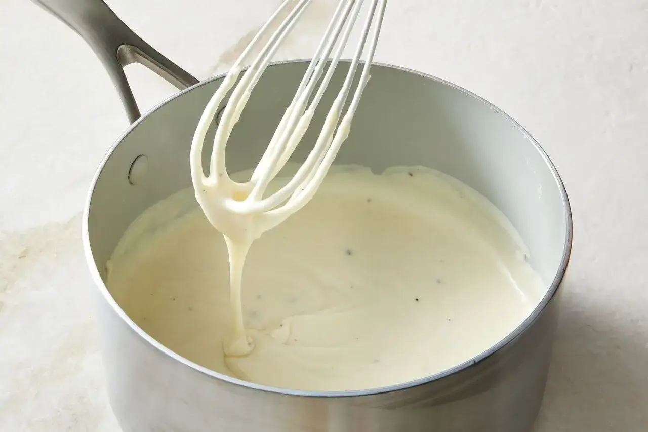 Cremige Bechamelsauce f&uuml;r Lasagne wird in einem Topf mit einem Schneebesen zubereitet.