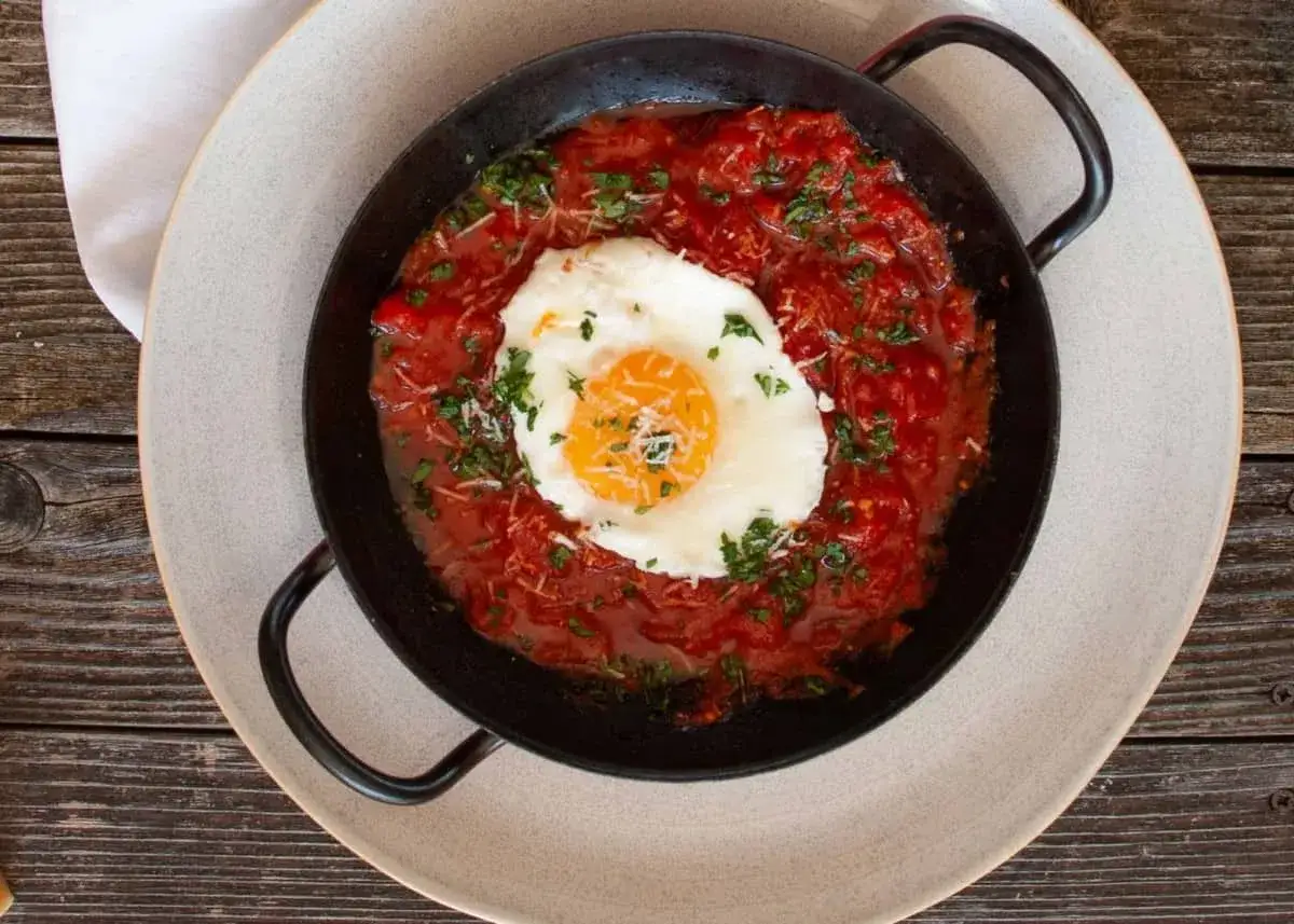 Uova in purgatorio: ein Spiegelei ruht auf einer würzigen Tomatensoße, garniert mit Petersilie und Parmesan.