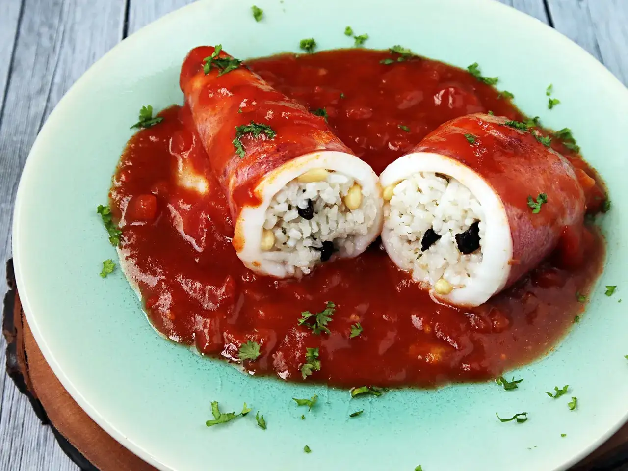 Zwei gefüllte Tintenfische (seppie ripiene) in Tomatensauce, gefüllt mit Reis, Pinienkernen und Oliven, garniert mit Petersilie.