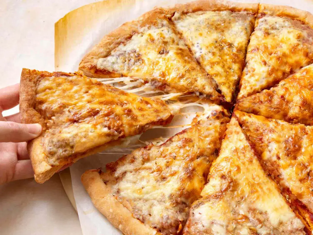 Eine Hand hebt ein Stück einer köstlichen Pizza mit geschmolzenem Käse an. Perfekt für einen schnellen Pizzateig!