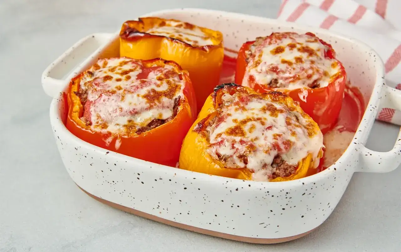 Vier bunte, gefüllte Paprika, überbacken mit geschmolzenem Käse, in einer Auflaufform. Köstliche Peperoni ripieni!