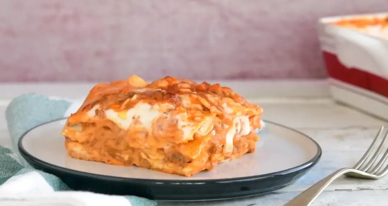 Ein Stück Lasagne al Ragu auf einem Teller, mit geschmolzenem Käse und einer Gabel daneben.