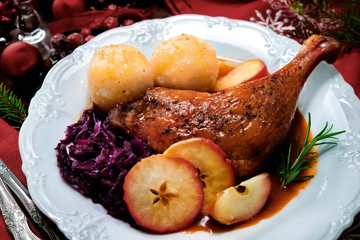 Festliches Gericht: knusprige Ente mit Klößen, Rotkohl und Apfelscheiben. Ein perfekter Wein zu Ente.