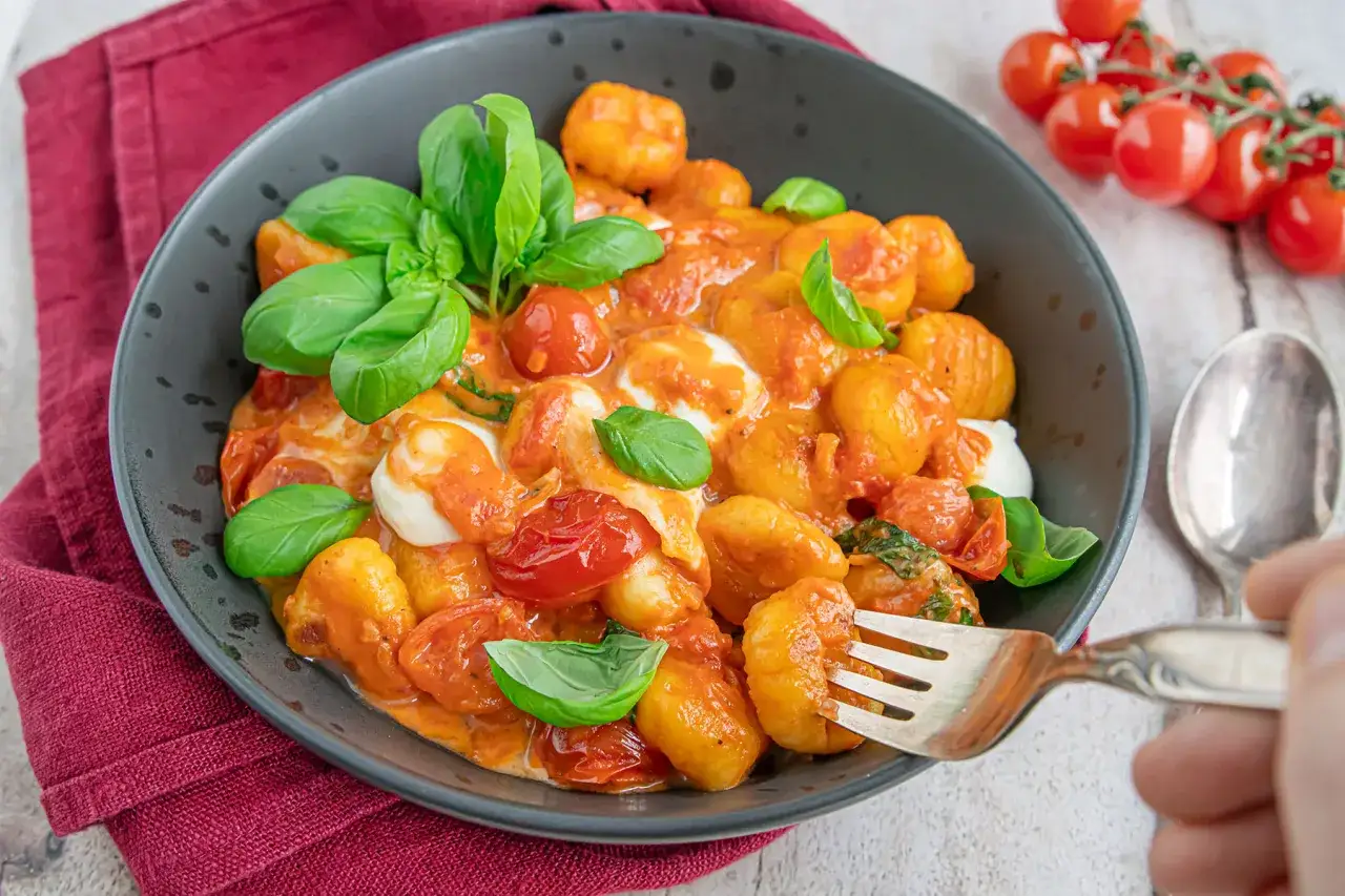 Gnocchi al forno mit Tomaten, Mozzarella und Basilikum in einer dunklen Sch&uuml;ssel, bereit zum Genie&szlig;en.