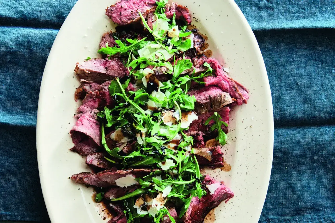 Ein perfekt gegrilltes Steak italienisch, belegt mit Rucola und Parmesan, beträufelt mit Balsamico-Glasur.