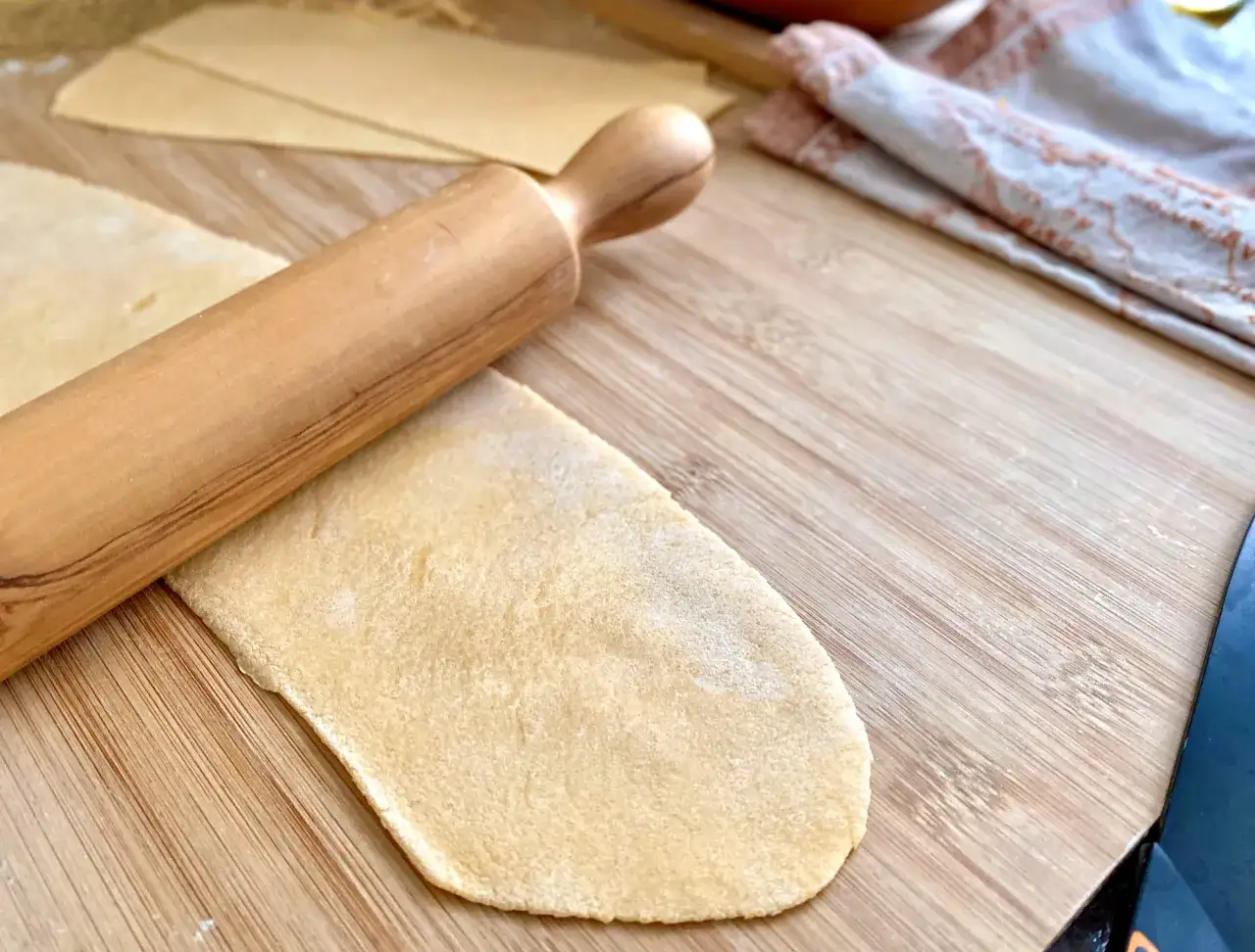 Ein Nudelholz rollt den frischen ravioli-teig rezept italienisch auf einem Holzbrett aus.