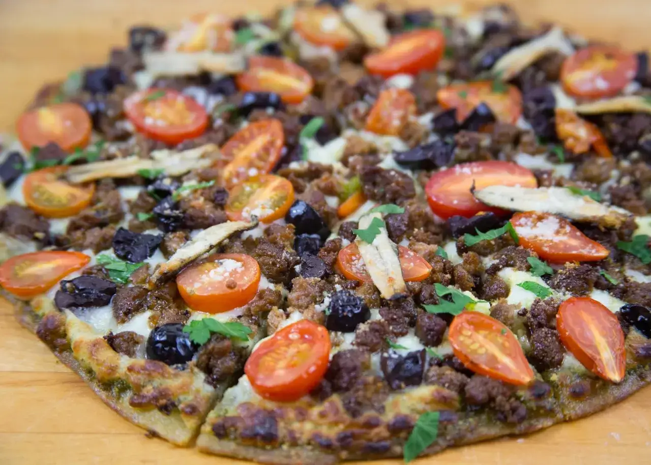Eine Sardellen Pizza mit Hackfleisch, Kirschtomaten und schwarzen Oliven, garniert mit Petersilie.