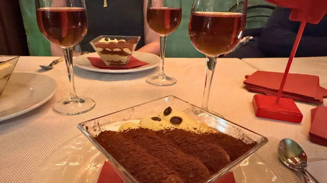 Drei Gläser mit süßem, bernsteinfarbenem italienischem Dessertwein stehen neben Tiramisu.