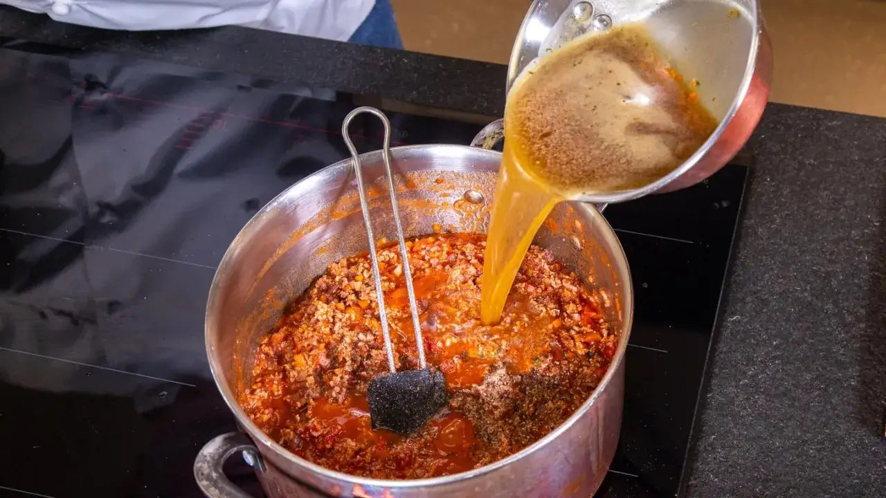 Flüssigkeit wird in einen Topf mit herzhaftem al ragu gegossen, um die Sauce zu verfeinern.