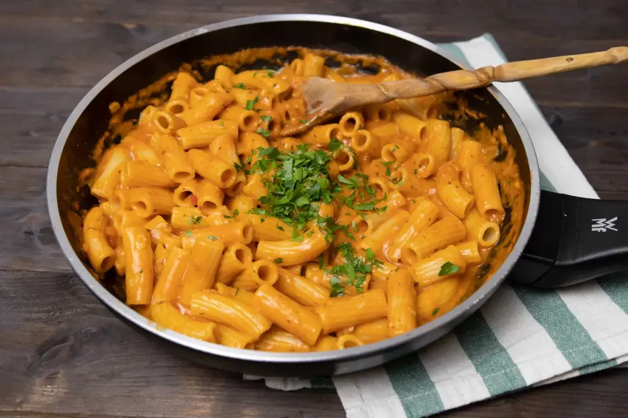 Herzhafte Rigatoni in cremiger Tomaten Sahne Sauce, garniert mit frischer Petersilie, bereit zum Servieren in einer Pfanne.