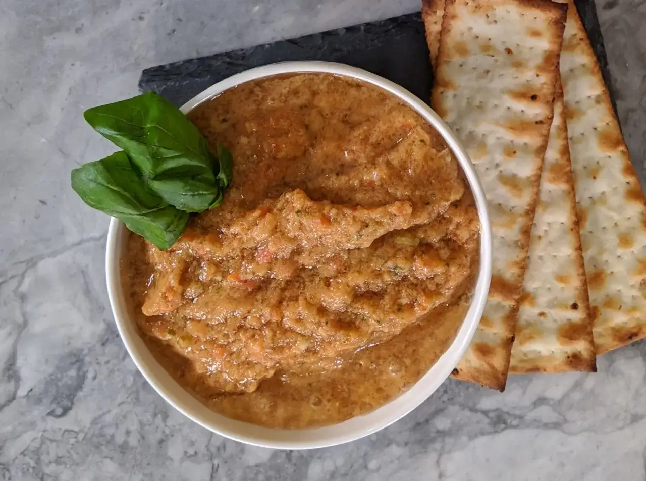 Ein cremiger Tomatendip, perfekt für Ihr nächstes Tomatendip Rezept, garniert mit frischem Basilikum und serviert mit knusprigen Crackern.