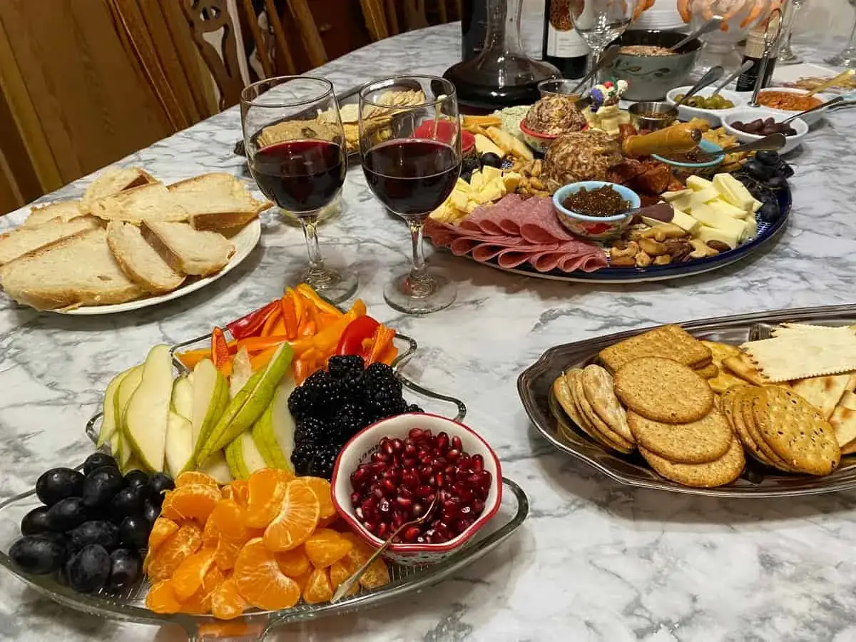Festliches Buffet mit K&auml;se, Wurst, Brot, Obst und zwei Gl&auml;sern fruchtiger Wein.