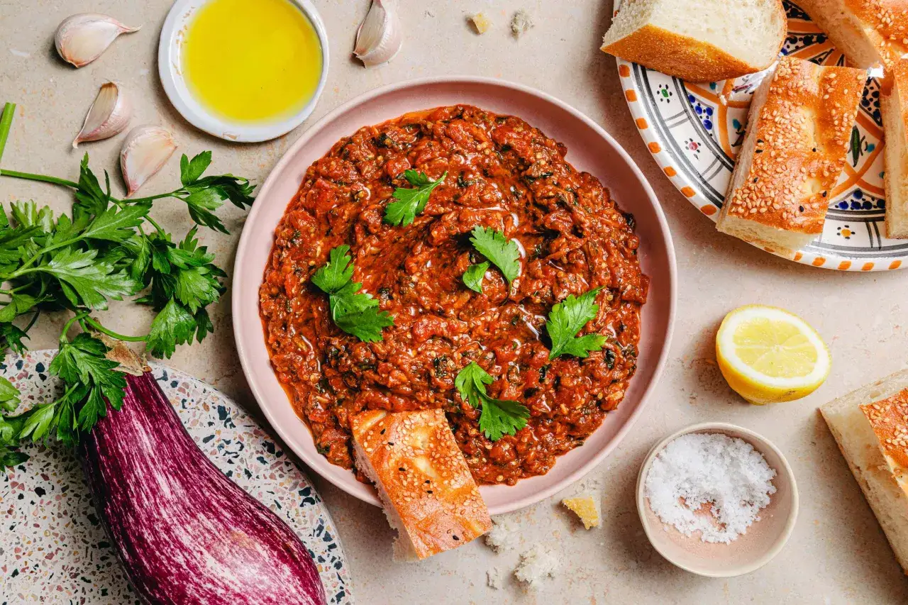 Herzhaft geschmorte Auberginen in Tomatensauce, garniert mit Petersilie, serviert mit Brot und Zitrone.