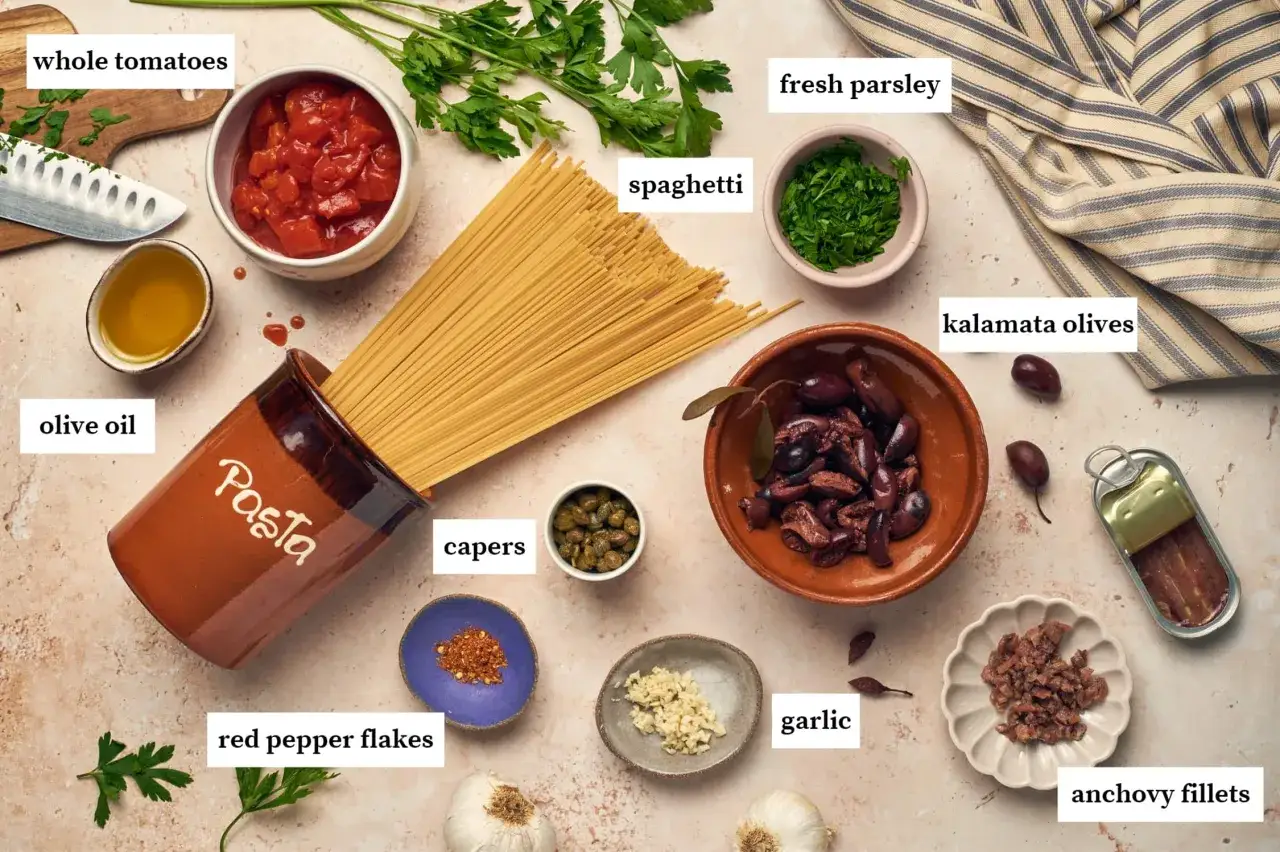 Zutaten f&uuml;r Spaghetti Puttanesca: Spaghetti, Tomaten, Oliven&ouml;l, Kapern, Knoblauch, Sardellen, Oliven, Petersilie und Chiliflocken.