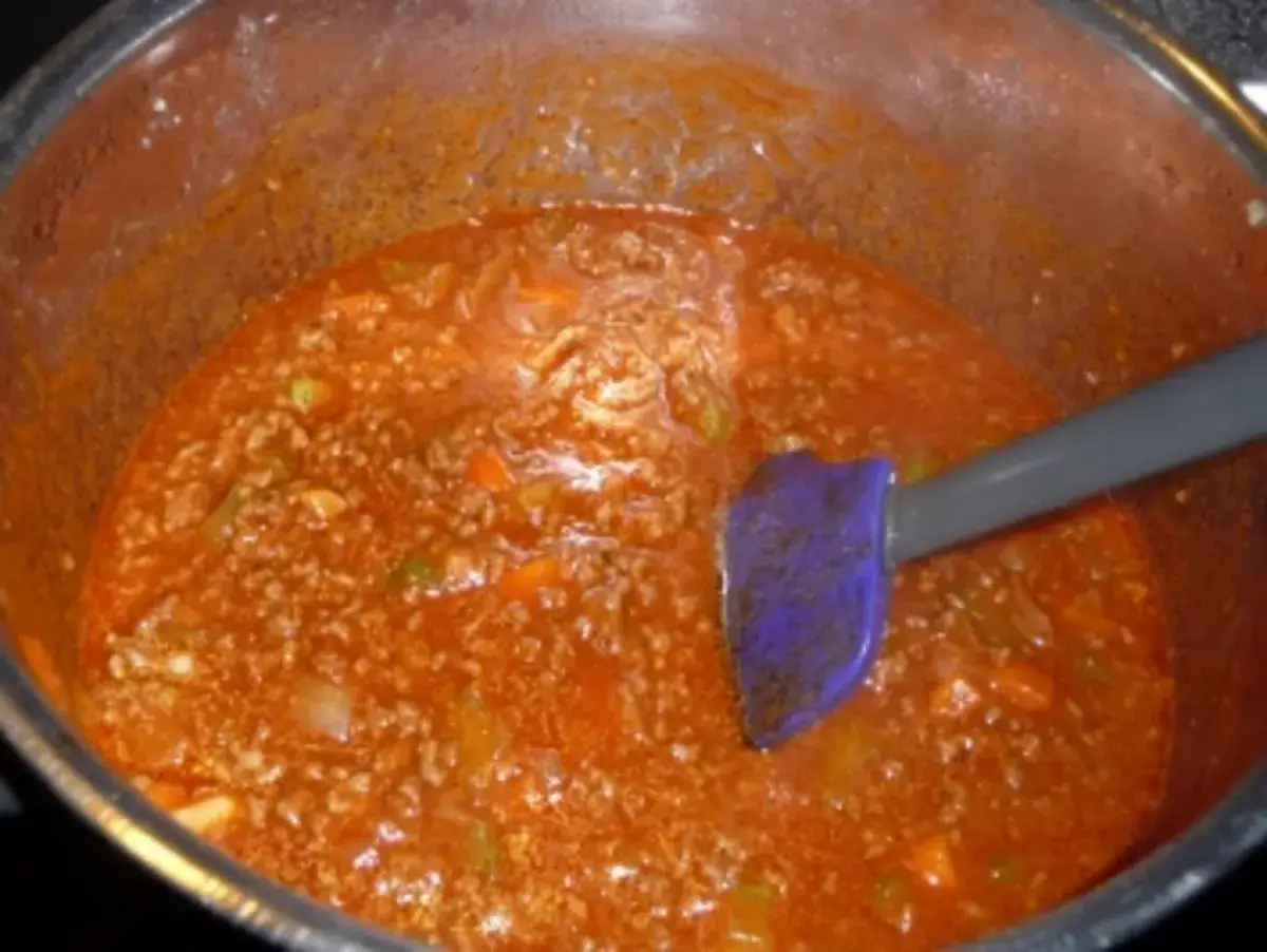 Eine köstliche, schnelle Bolognese köchelt in einem Topf. Ein lila Spatel rührt die herzhafte Sauce um.