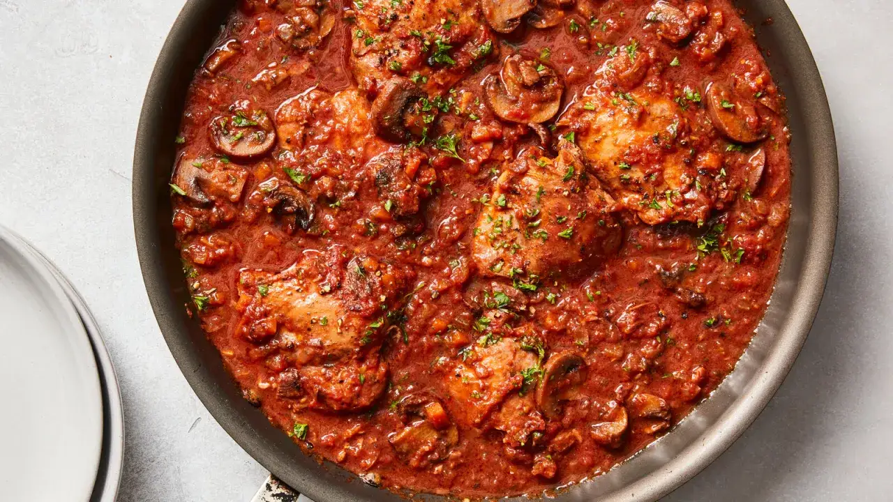 Herzhaftes Pollo Cacciatore in einer reichhaltigen Tomaten-Pilz-Sauce, garniert mit Petersilie, in einer Bratpfanne.