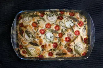 Frisch gebackene Focaccia mit Kirschtomaten, Zwiebelringen und Kräutern belegen.